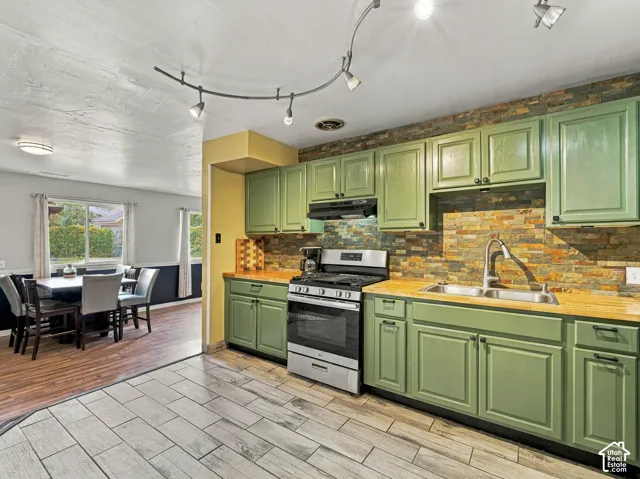 Kitchen featuring green cabinetry, wood-finish countertops, a stainless steel range, and a stacked stone backsplash