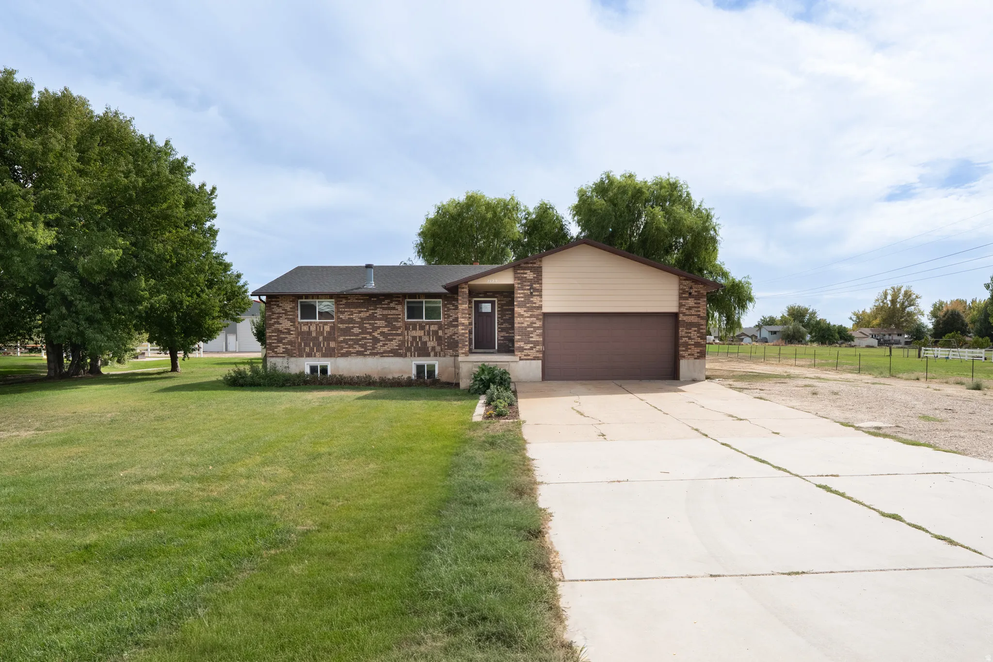Brick and siding exterior with an attached garage, featuring a concrete driveway and mature trees