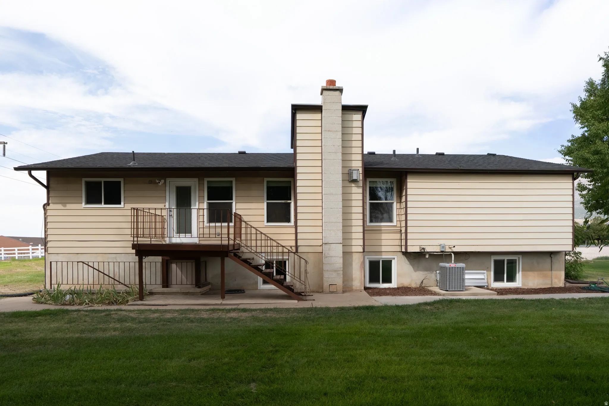 Rear exterior with tan siding, black shingle roof, and a deck with metal railings