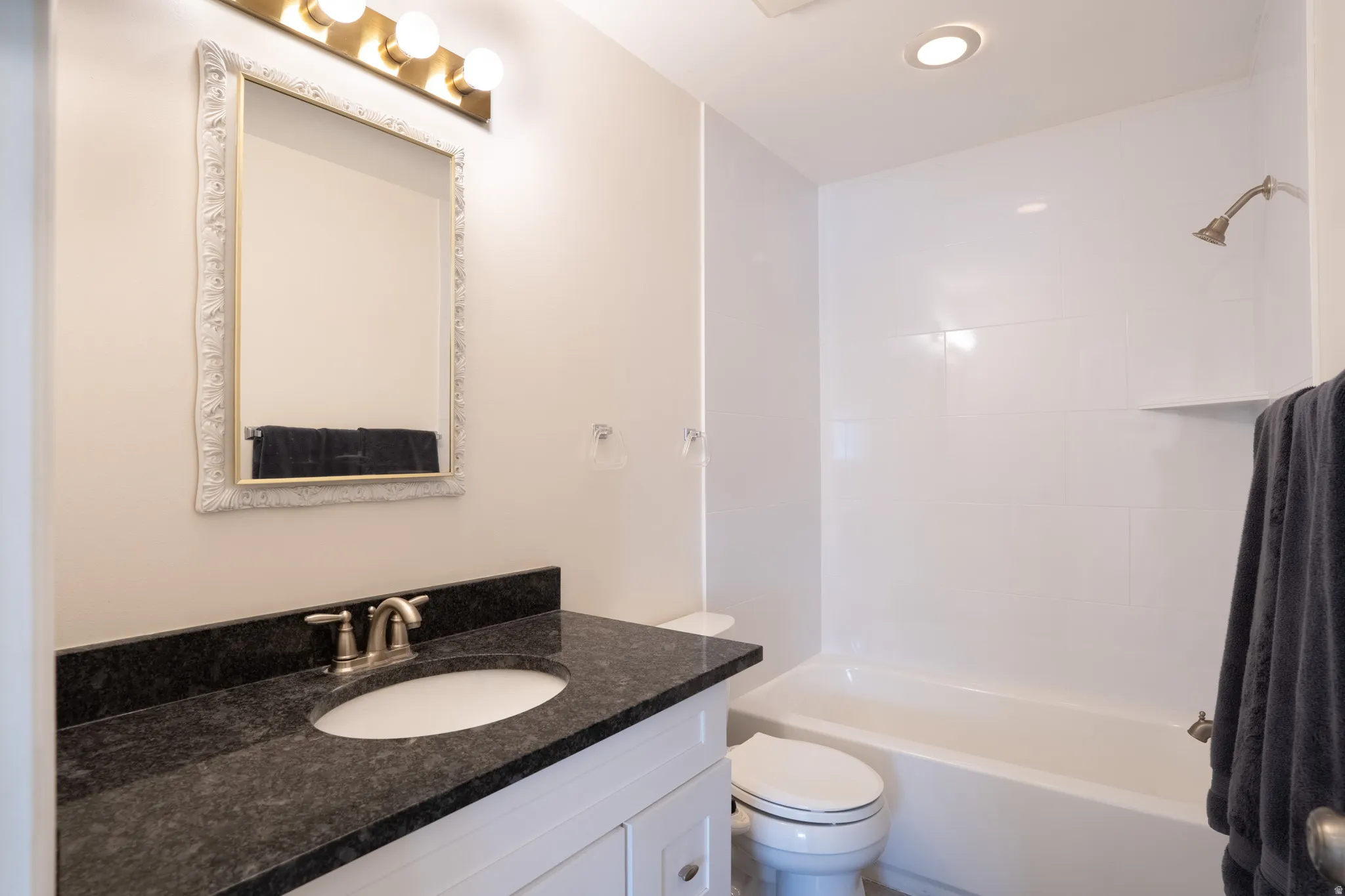 White vanity with a dark stone countertop and undermount sink and new tiled shower