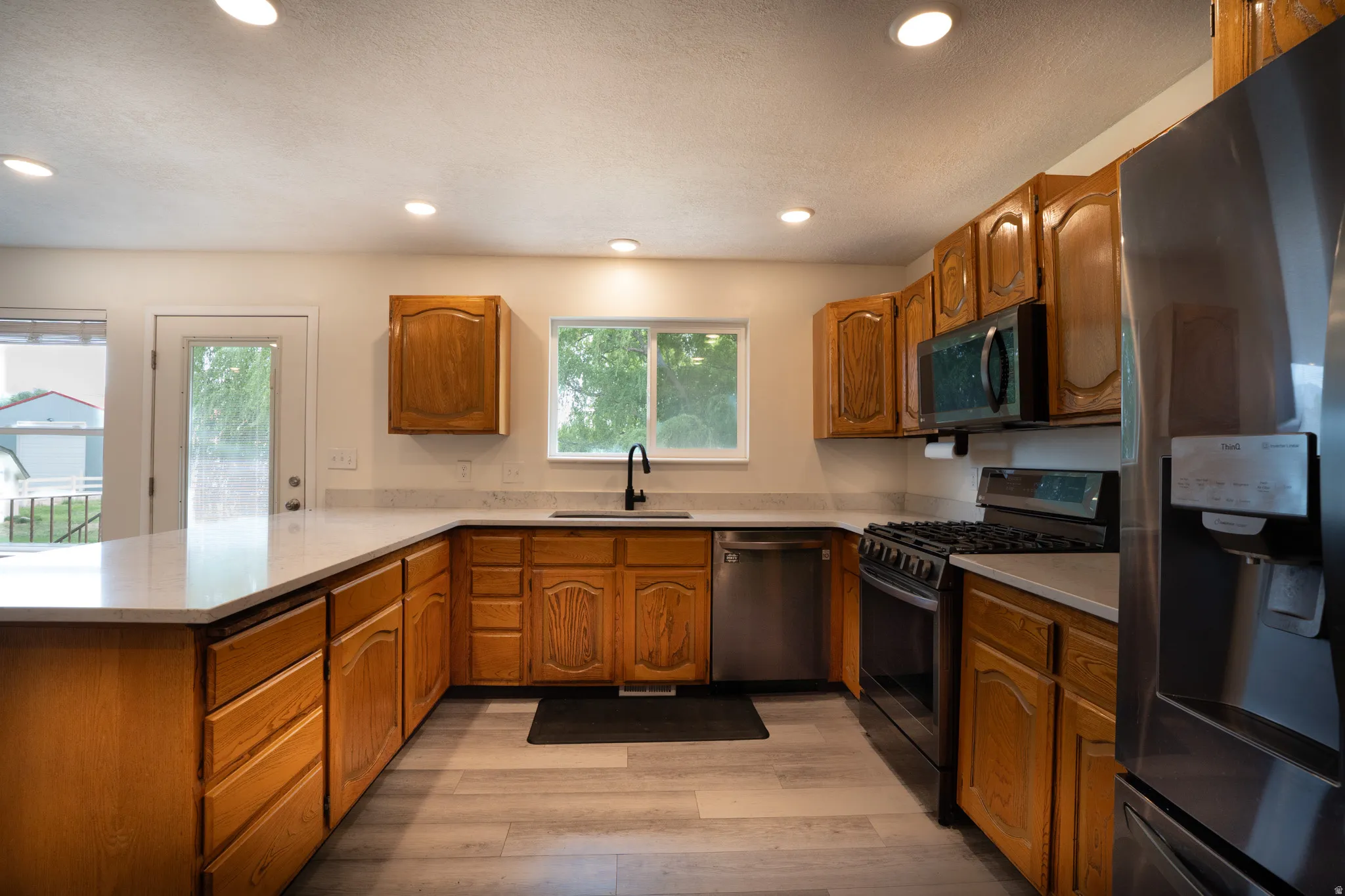 U-shaped kitchen featuring wood cabinetry, light-toned countertops, and new appliances