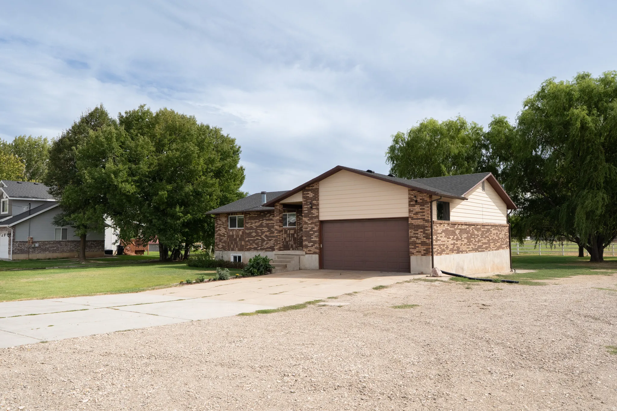 Split-level residence featuring a two-car garage, brick and siding exterior, concrete driveway, and mature landscaping