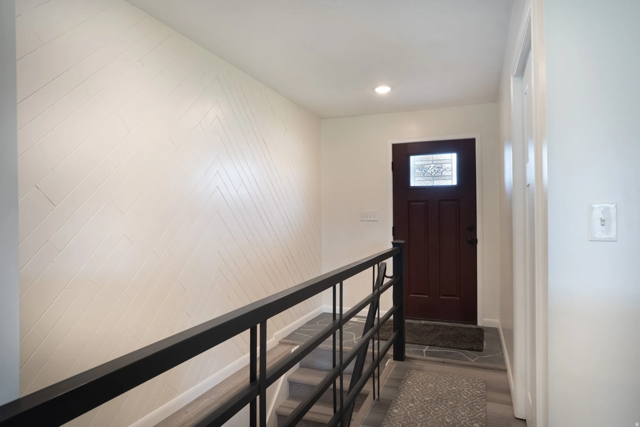 Herringbone-patterned accent wall, updated flooring, front door, and railing.
