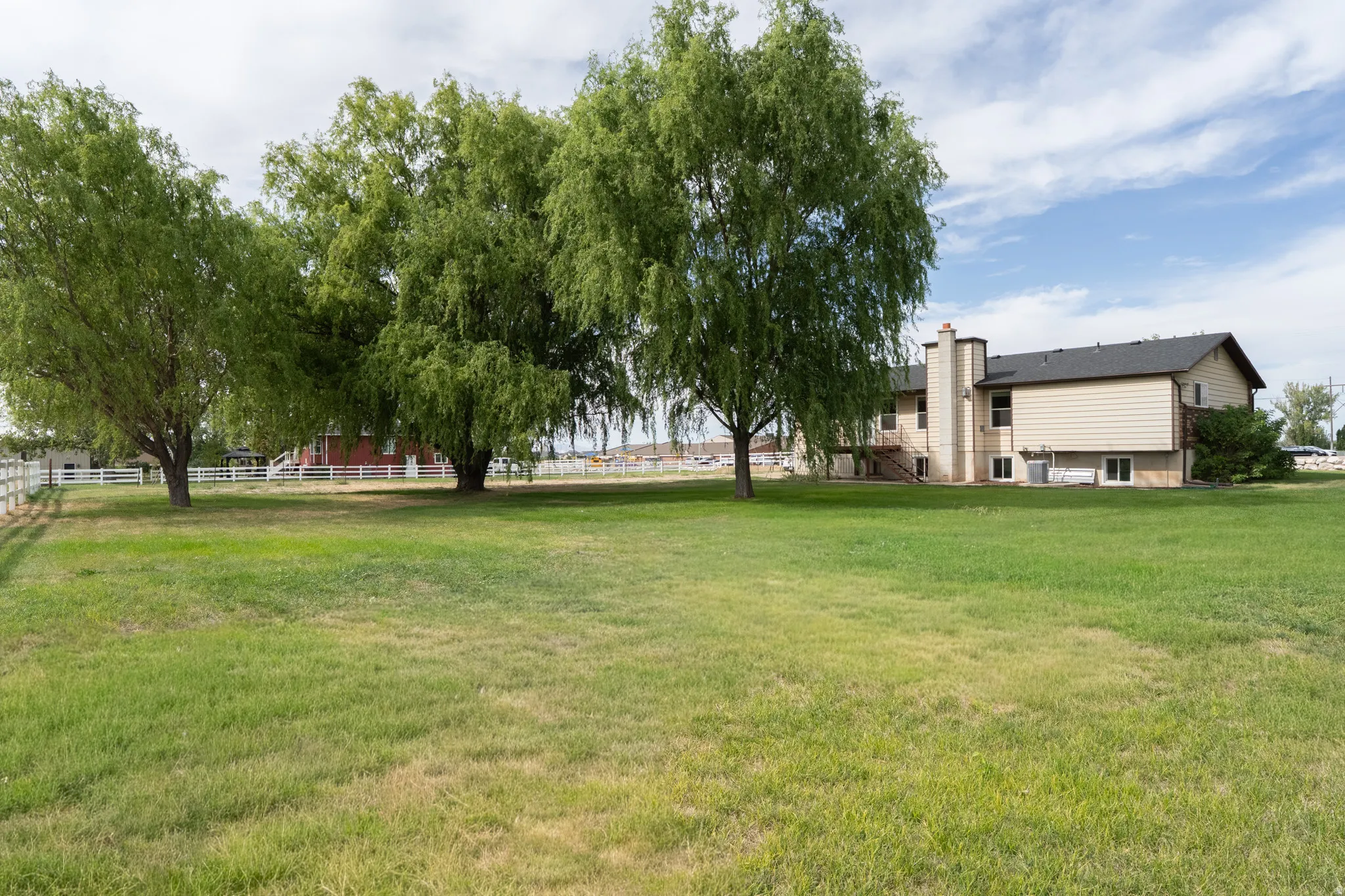 Expansive lawn with mature trees and a white picket fence for backyard.