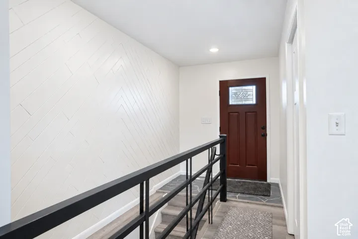 Herringbone pattern wall paneling, dark wood entry door with decorative glass inlay, black metal staircase railing, and recessed ceiling lighting