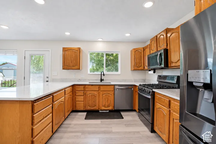 U-shaped kitchen featuring wood cabinetry, light-toned countertops, stainless steel appliances, and wood-finish flooring