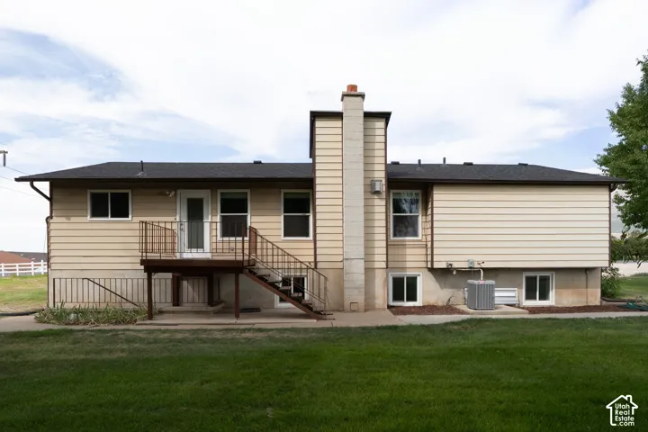 Rear exterior with tan siding, black shingle roof, and a deck with metal railings