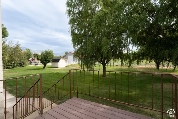 Trex deck with railing. Expansive lawn with mature trees, a detached shed, mountain backdrop, and a brown wood-finish deck with metal railings