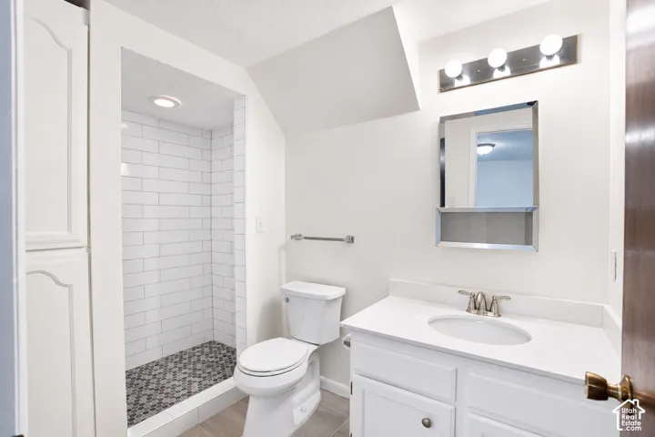 Remodeled bathroom with walk-in shower, subway tile surround and mosaic tile floor, white vanity with integrated sink and chrome faucet, and built-in storage cabinetry