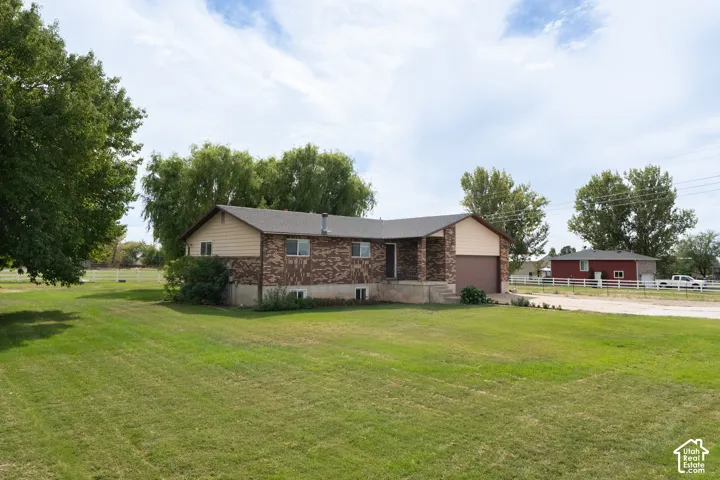 Spacious lawn with mature trees, a brick and siding exterior, an attached garage, and a covered front entry