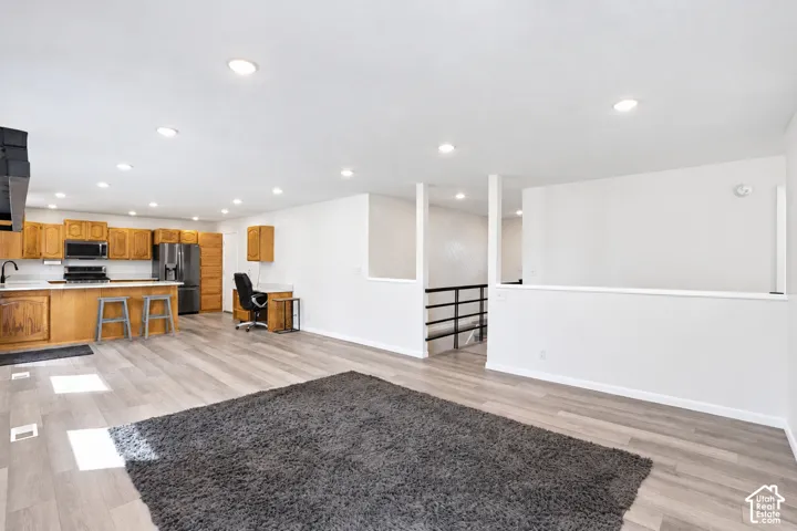 Open-concept living area featuring wood-finish flooring, recessed lighting, a kitchen with wood cabinetry, and a black railing system