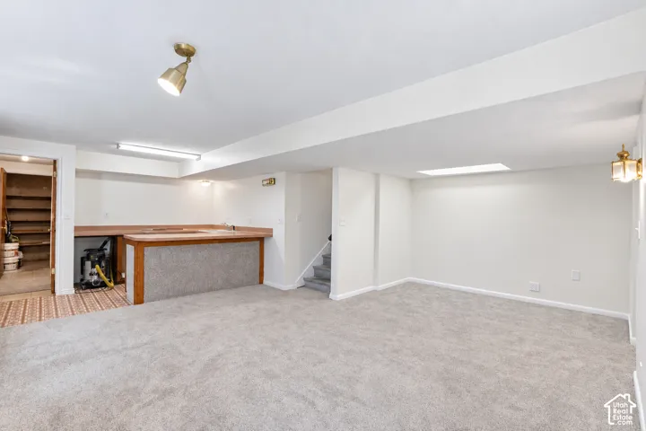 Spacious room with light-toned carpet, a built-in bar with wood-finish countertop, and overhead lighting