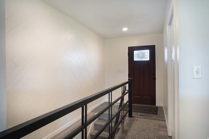 Herringbone-patterned accent wall, updated flooring, front door, and railing.