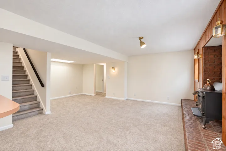 Carpeted room with a central staircase, built-in wood-burning stove on a brick hearth, and wood paneling accents