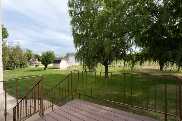 Trex deck with railing. Expansive lawn with mature trees, a detached shed, mountain backdrop, and a brown wood-finish deck with metal railings