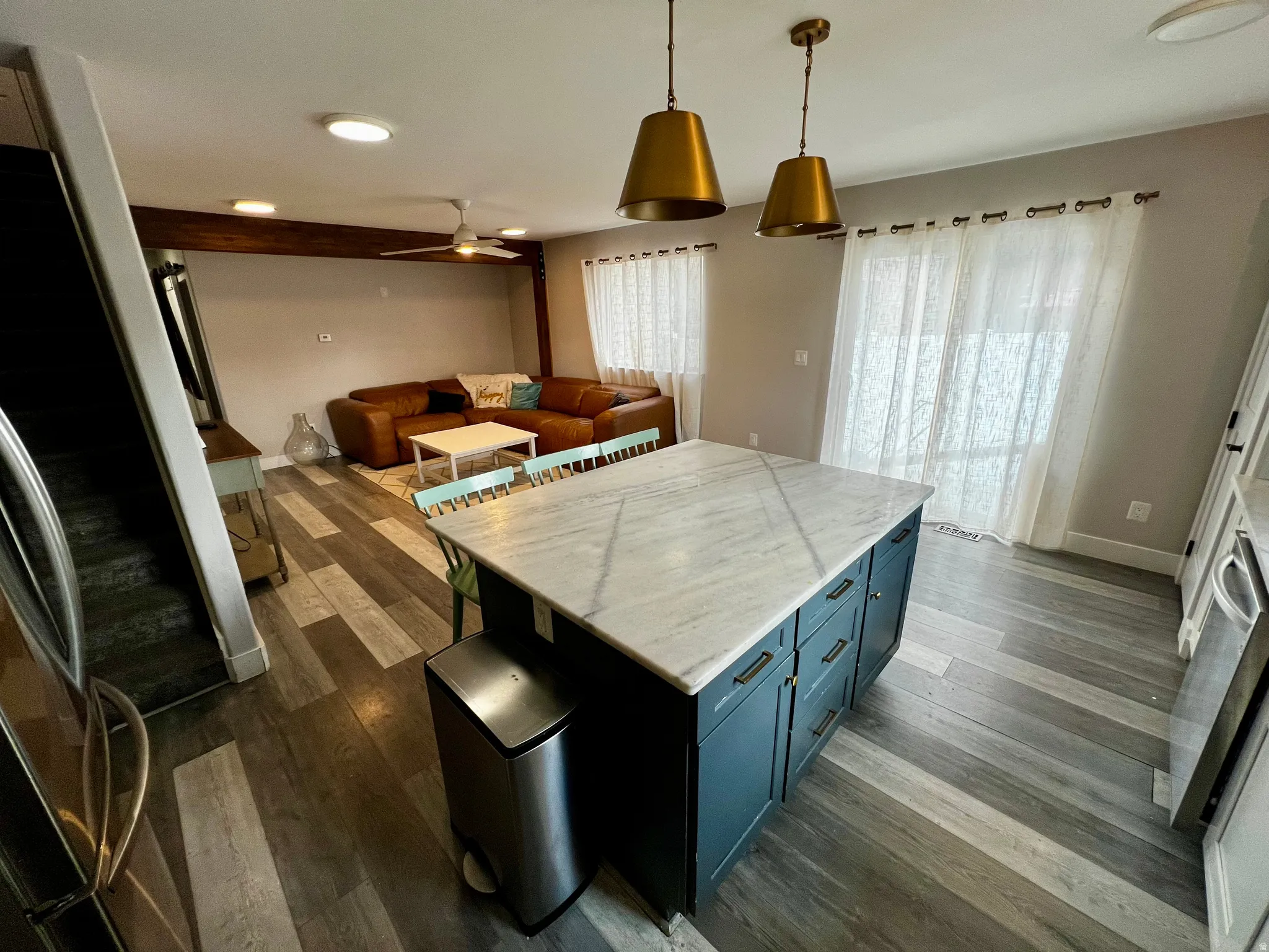 Kitchen island with a light-toned countertop, pendant lighting, wood-finish flooring, and a ceiling fan