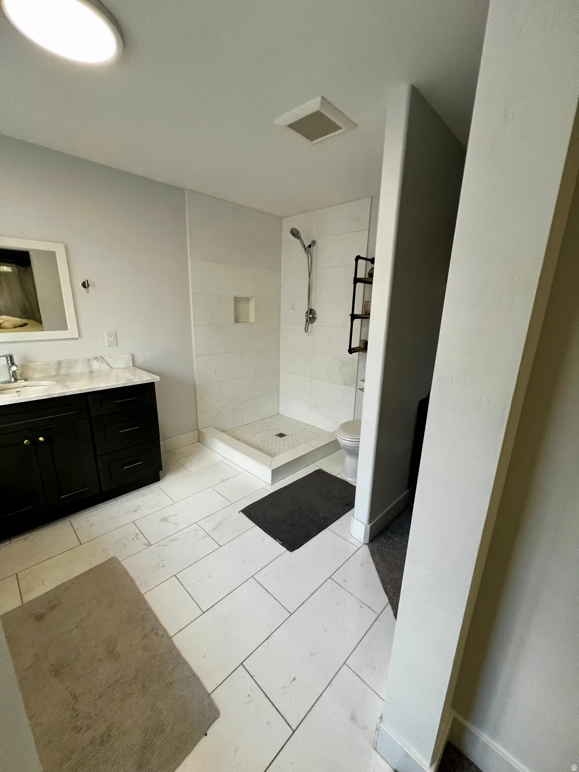 Bathroom featuring white rectangular floor tiles and a walk-in shower with a tiled surround