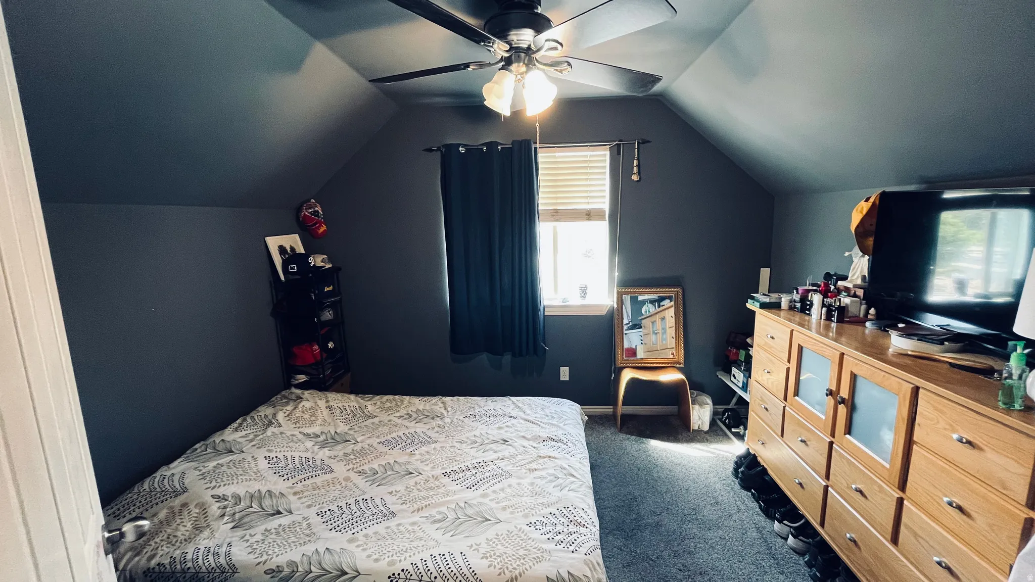 Sloped ceiling room featuring a ceiling fan with integrated lighting, a window with blinds, and carpeting