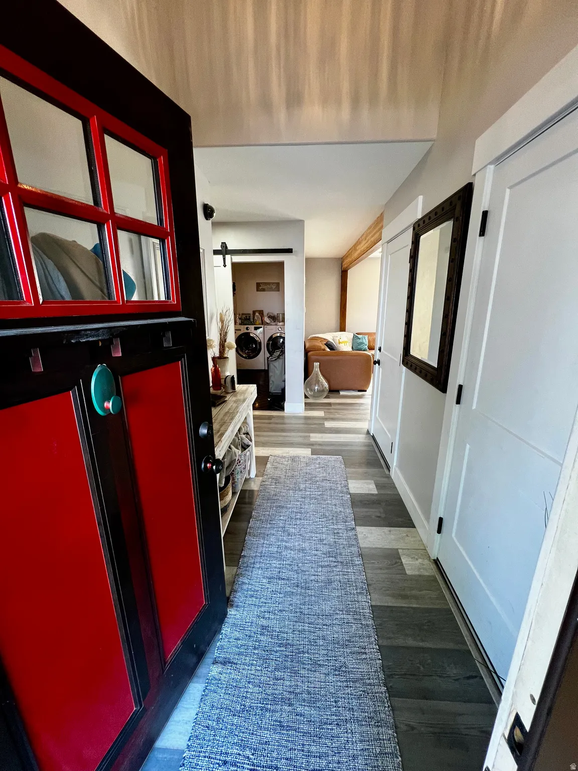 Vibrant red entry door with window panes, wood-finish flooring, white paneled interior doors, and a built-in shelf with a wood countertop