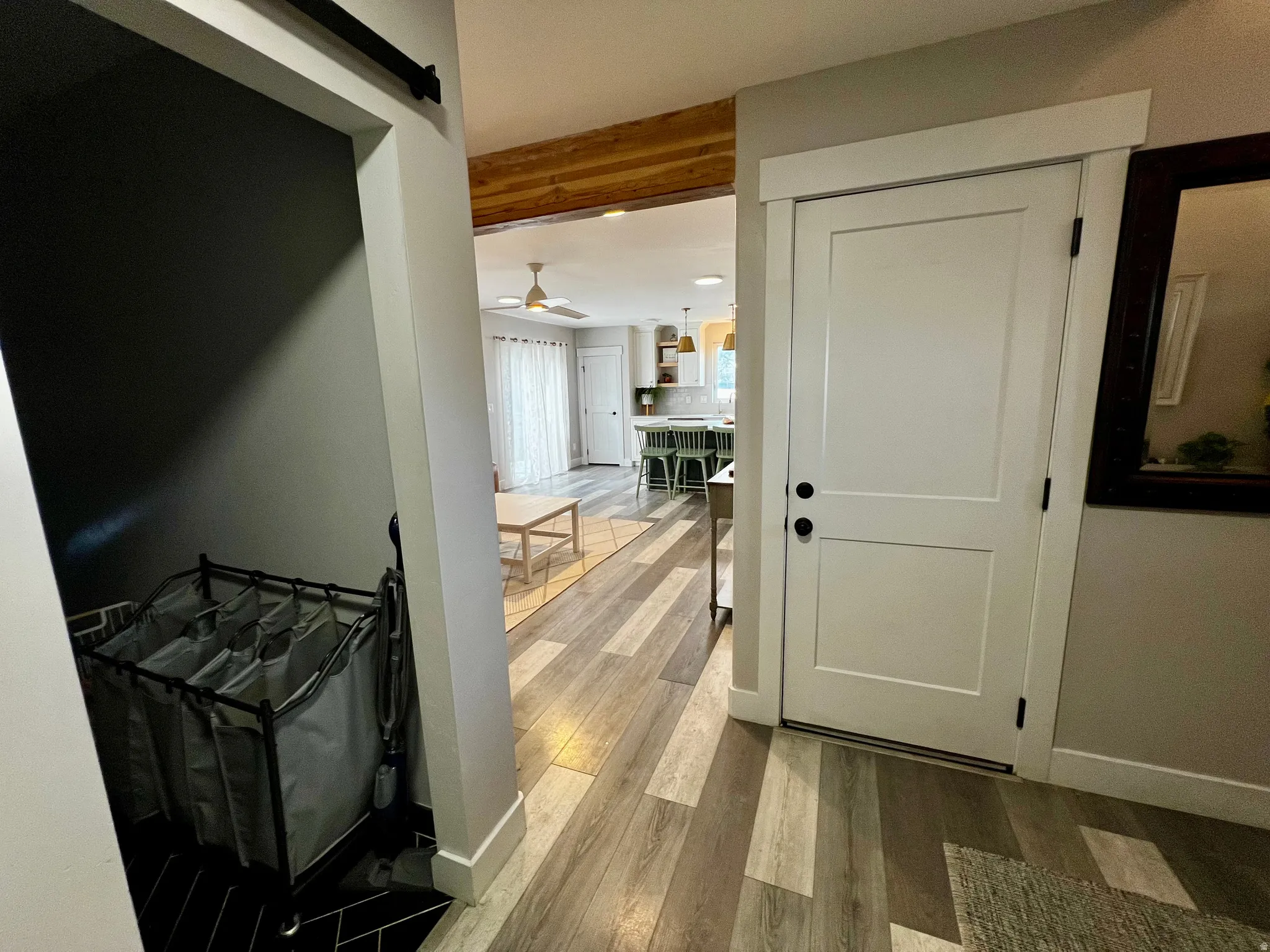 Barn door entry, wood-finish flooring, white paneled interior door, dark hardware, exposed wood beam