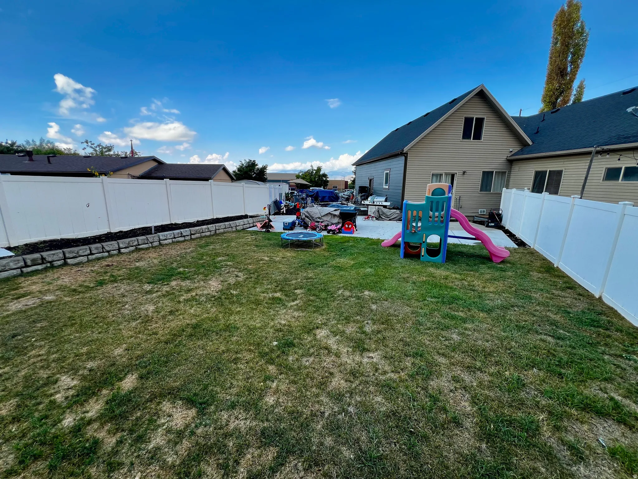 Expansive backyard featuring a privacy fence, a retaining wall, and a large paved patio area