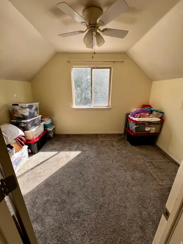 Carpeted room featuring sloped ceilings, a ceiling fan with integrated lighting, and a single window