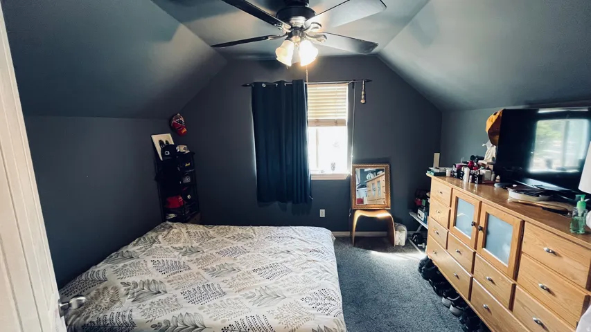 Sloped ceiling room featuring a ceiling fan with integrated lighting, a window with blinds, and carpeting