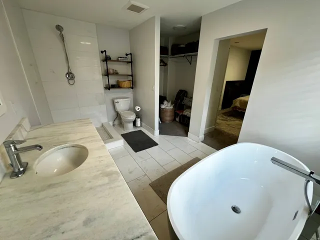 Freestanding soaking tub, walk-in shower with tiled surround, single vanity with stone countertop, and tile flooring