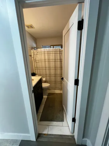 Bathroom featuring white square floor tiles, a dark wood-finish vanity with a light-colored countertop, and a white toilet
