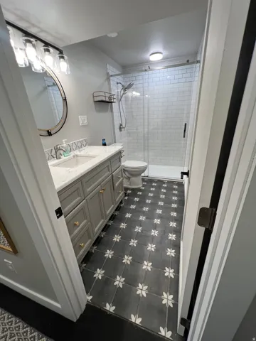Bathroom featuring a single vanity with stone countertop, patterned floor tile, subway tile shower surround, and a glass-enclosed shower
