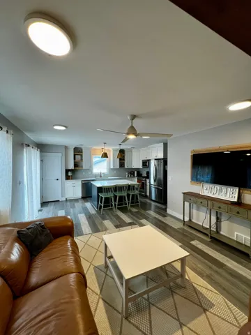 Open-concept living space with wood-finish flooring, white cabinetry, a kitchen island, pendant lighting, and stainless steel appliances