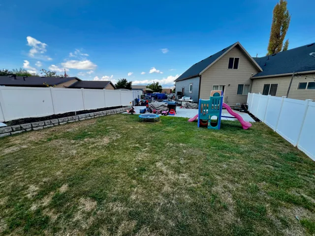Expansive backyard featuring a privacy fence, a retaining wall, and a large paved patio area