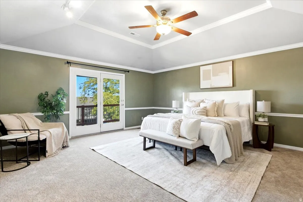 Vaulted ceiling with crown molding, ceiling fan, carpet flooring, wall paneling, and double French doors to exterior balcony