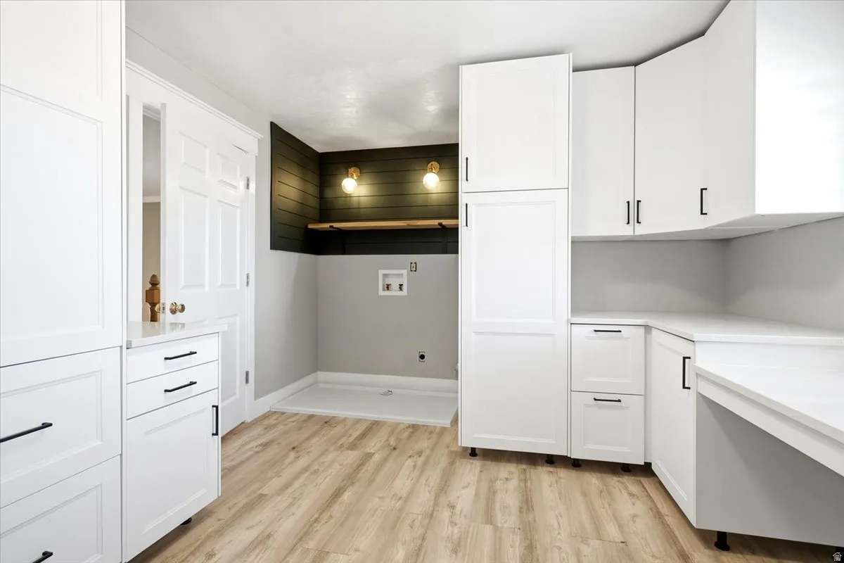 Integrated laundry area featuring wood-finish flooring, white cabinetry, dark accent wall paneling, and a built-in shelf