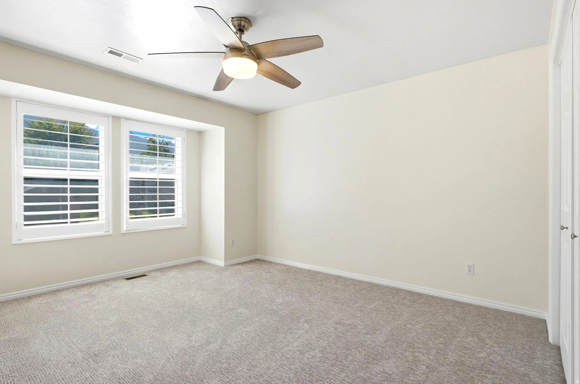 Recessed window alcove with plantation shutters, ceiling fan with integrated lighting, neutral-toned wall paint, and carpeted flooring