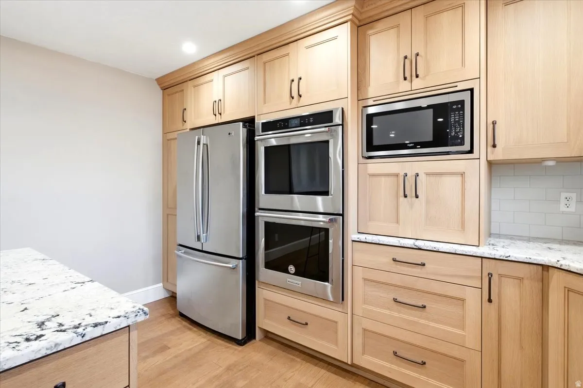Custom cabinetry with dark bronze hardware, stainless steel appliances, double wall ovens, integrated microwave, and white speckled countertops