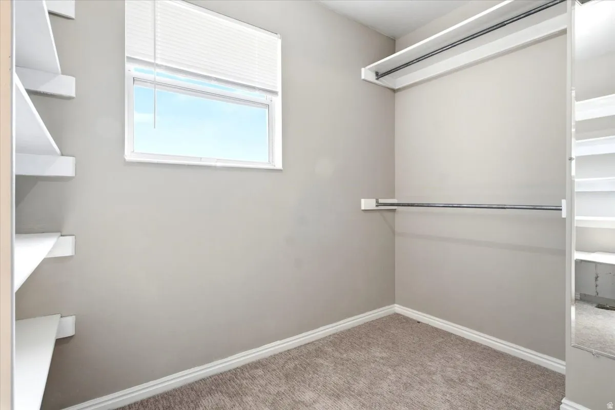 Walk-in closet featuring built-in shelving, hanging rods, and a window with blinds