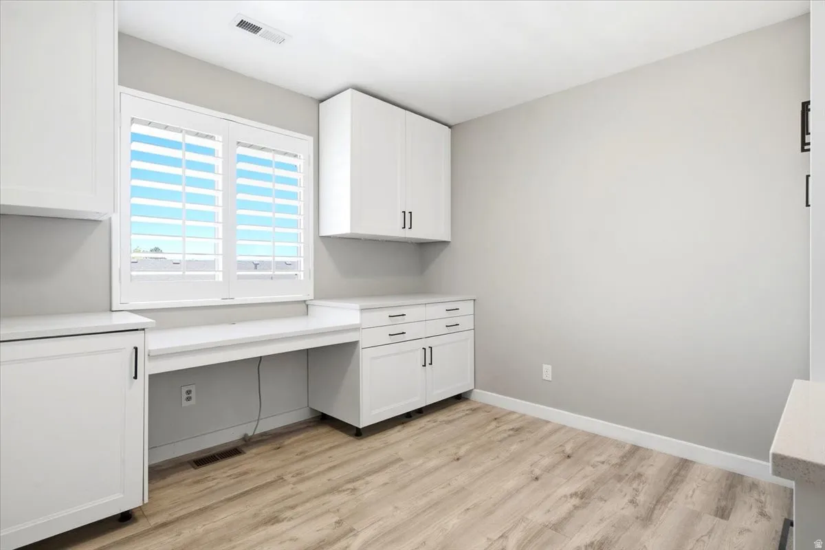 Built-in desk area with white cabinetry, light-toned countertops, and wood-finish flooring