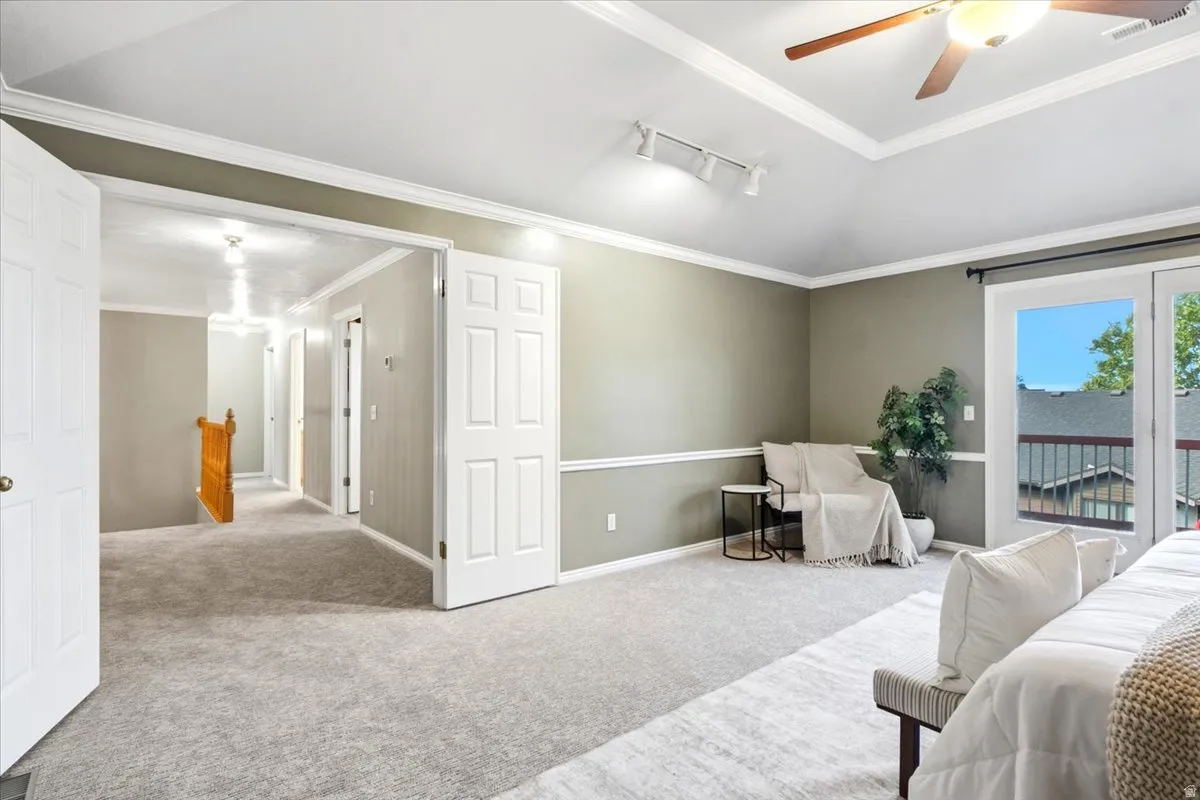 Carpeted room featuring a vaulted ceiling with a fan, crown molding, and wainscoting