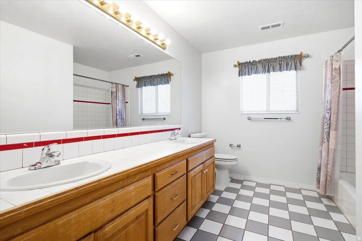 Dual vanity with wood-finish cabinetry, a large wall-mounted mirror, and checkered floor tiling
