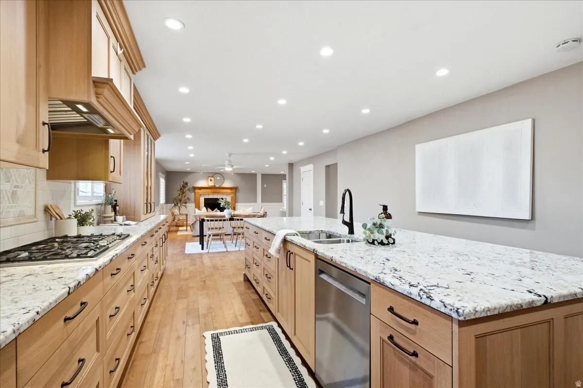Full-width kitchen featuring light wood cabinetry, stone countertops, integrated gas range, and a stainless steel dishwasher
