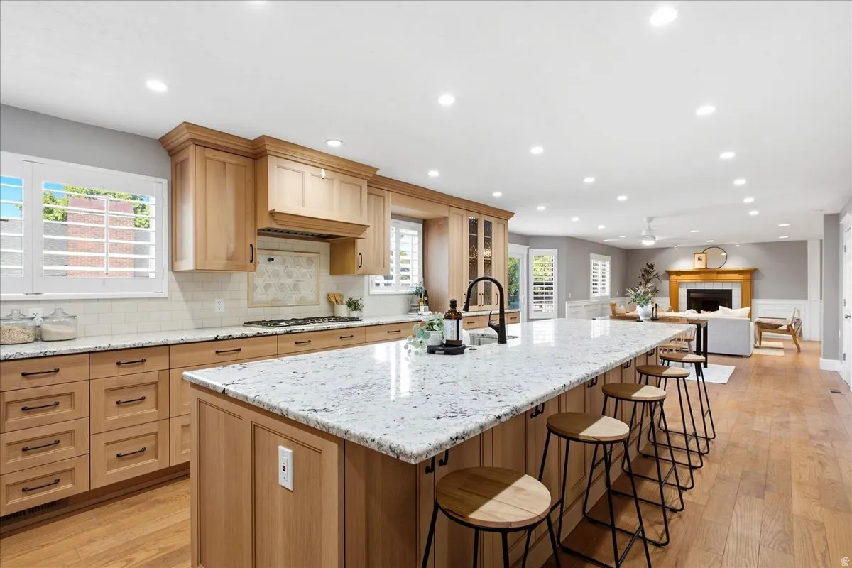 Expansive kitchen island with seating, natural wood-finish cabinetry, light-toned countertops, subway tile backsplash, and wide plank wood-finish flooring