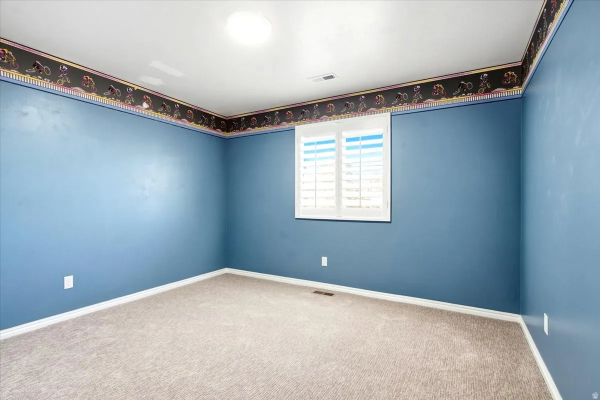 Carpeted room with a ceiling-mounted light fixture and a window with plantation shutters