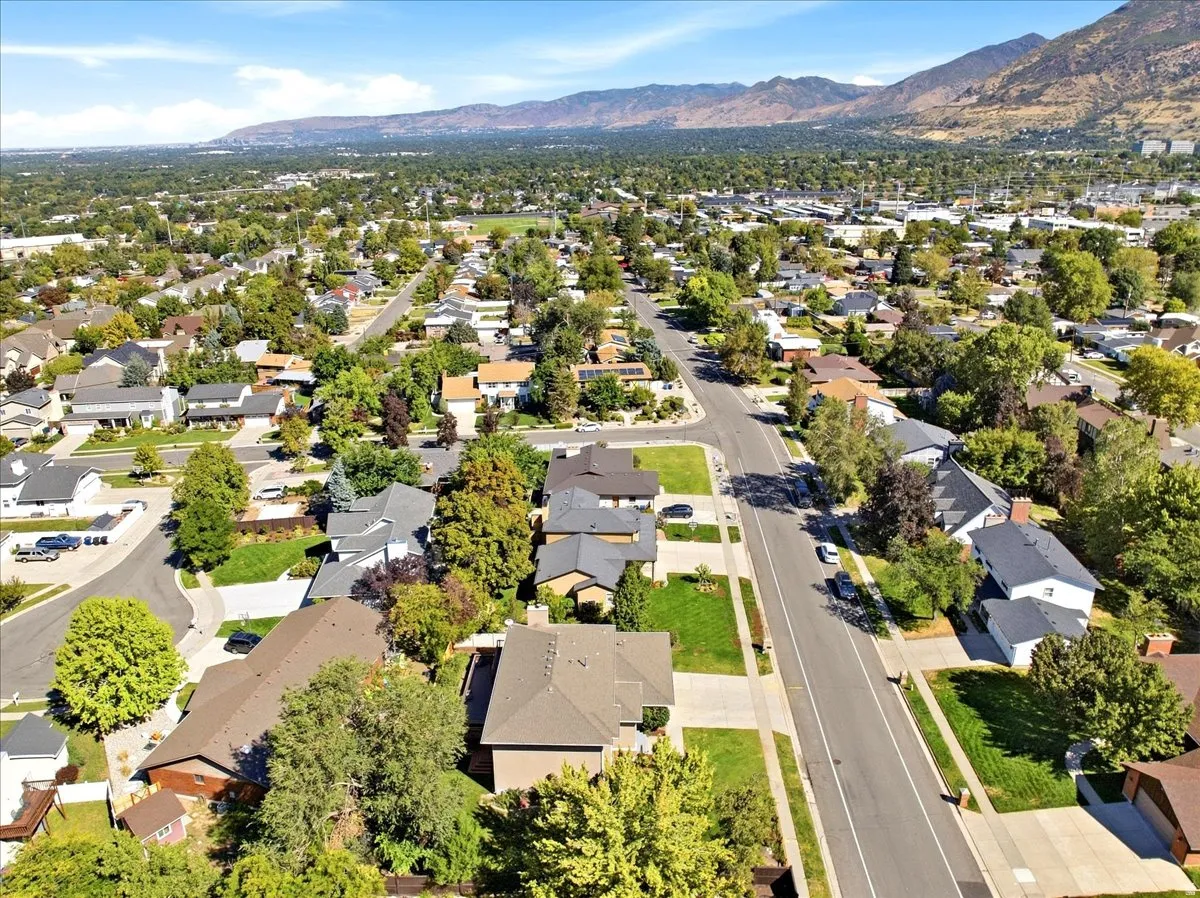 Residential neighborhood with mature trees, paved streets, and sidewalks, set against a distant mountain range