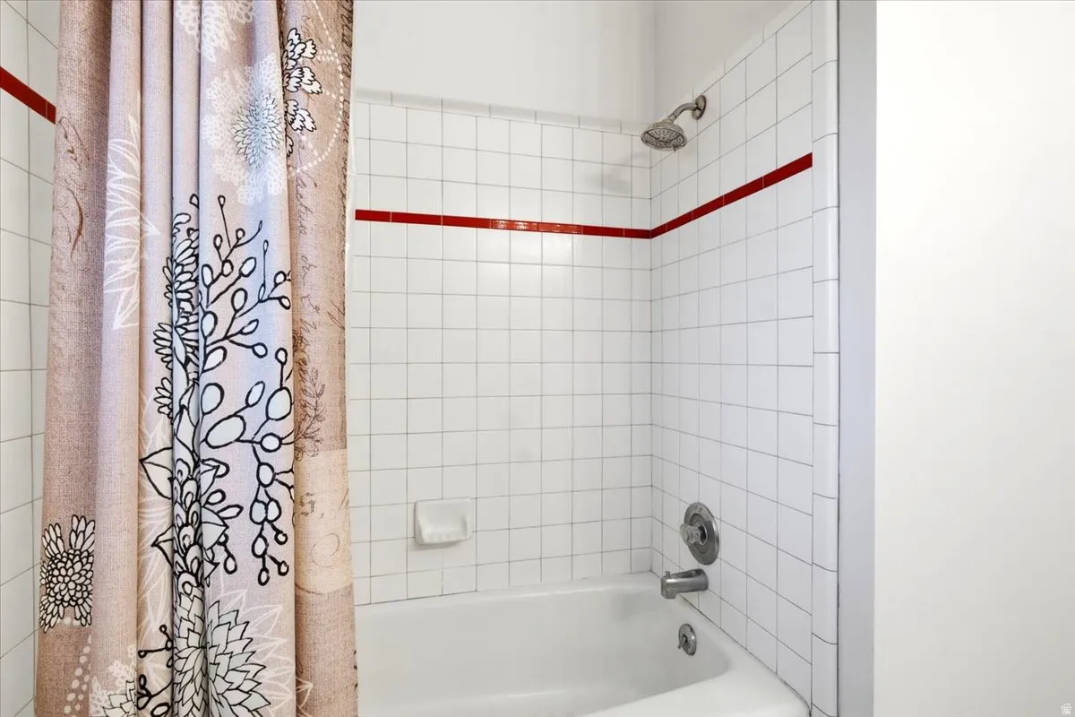 White tiled shower surround with a red accent stripe, featuring a chrome shower head and bath fixtures