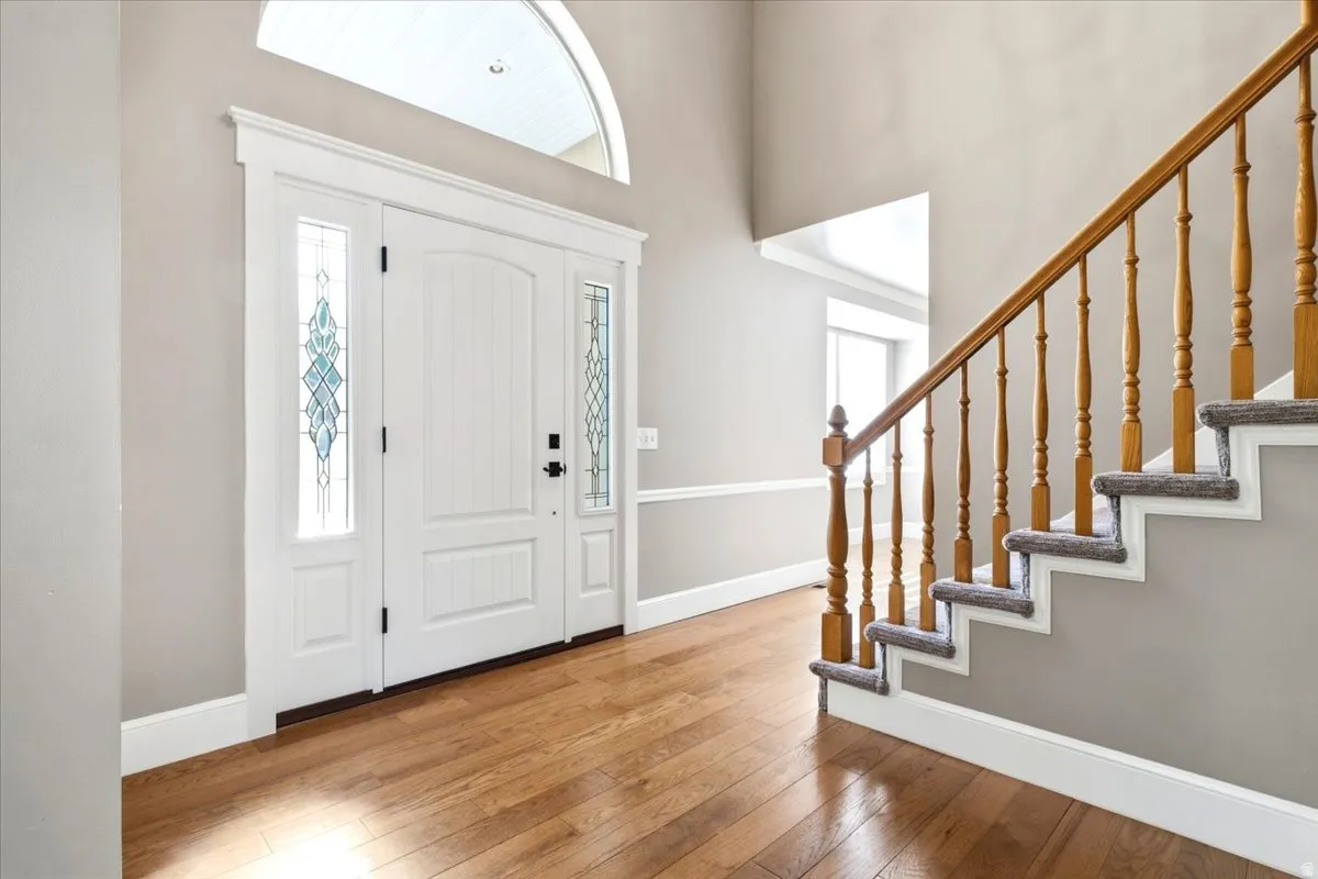 Hardwood-finish flooring, a grand entry door with decorative glass sidelights, an arched transom window, a two-story foyer, and a staircase with wood newel posts and spindles