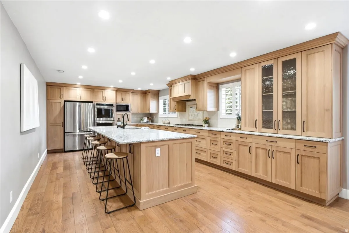Well-appointed kitchen featuring wood-finish cabinetry, stainless steel appliances, a center island with countertop seating, recessed lighting, and wood-finish flooring