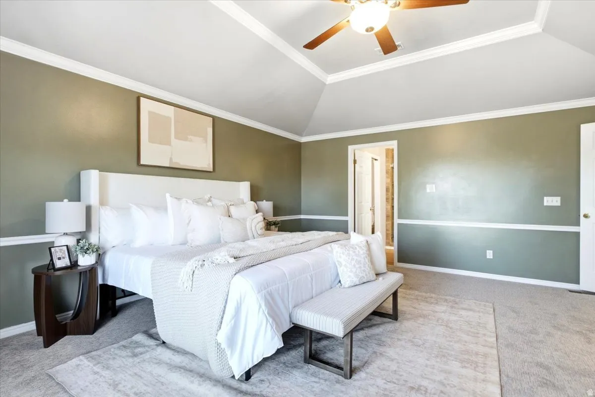 Vaulted ceiling with a ceiling fan, crown molding, two-tone painted walls, and carpet flooring