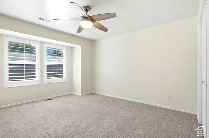 Recessed window alcove with plantation shutters, ceiling fan with integrated lighting, neutral-toned wall paint, and carpeted flooring