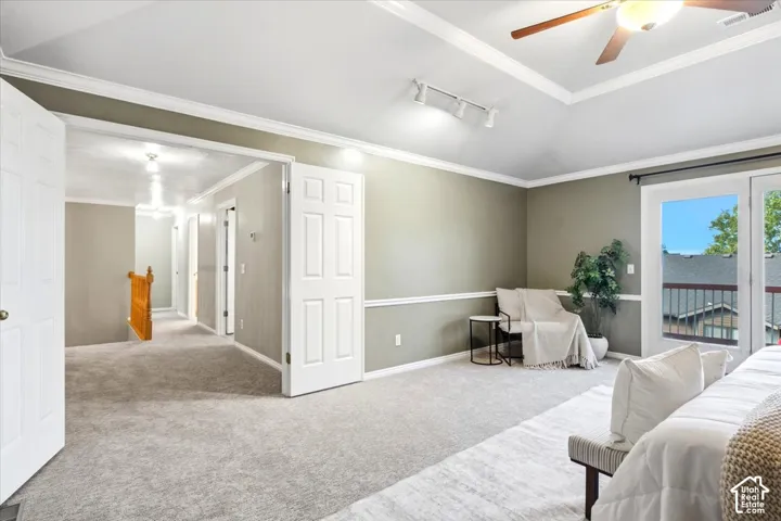 Carpeted room featuring a vaulted ceiling with a fan, crown molding, and wainscoting